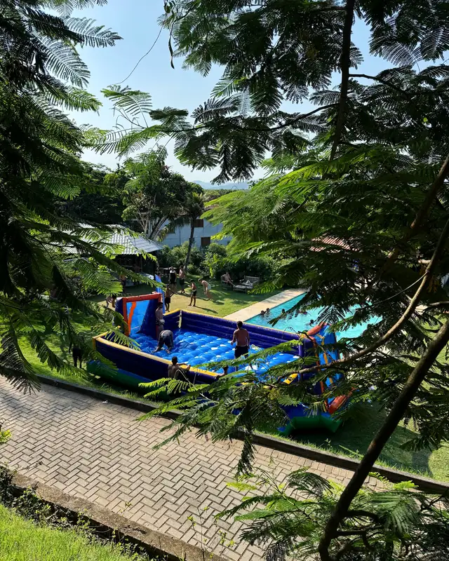 Vista do sítio do Follow Camp 2026, com piscina e brinquedo inflável entre as árvores